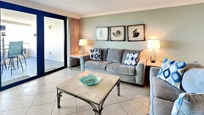 A living room with a sofa, two side tables, a coffee table, and a view of the outside. - Edgewater #611 | Beach Access, Pool, Gym, Hot Tub, Grills + More (Miramar Beach)