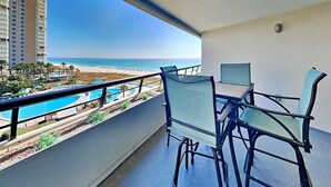 A balcony with a table and chairs, overlooking a beach and a swimming pool. - Edgewater #611 | Beach Access, Pool, Gym, Hot Tub, Grills + More (Miramar Beach)