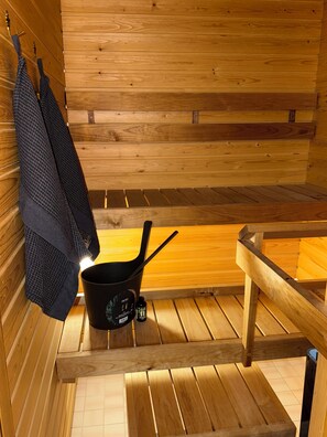 Eine Sauna mit Holzbänken, einem schwarzen Ofen und einem Handtuch an der Wand.