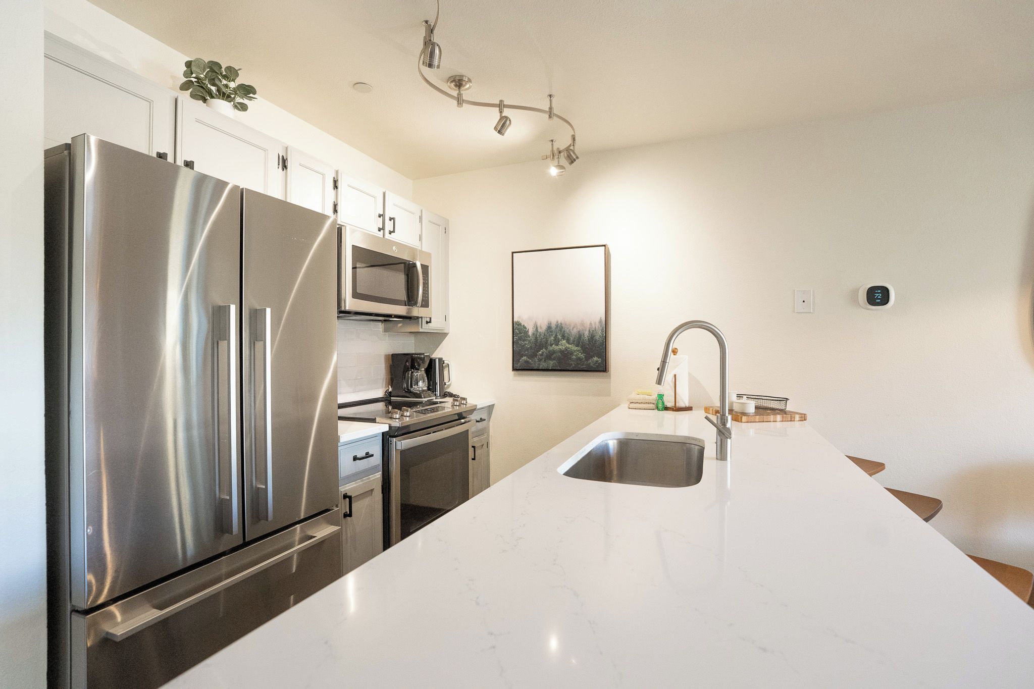 A modern kitchen with stainless steel appliances, a large island with a sink, and a framed picture on the wall.