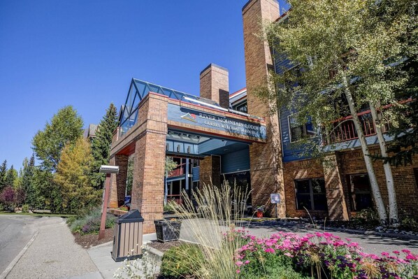A modern building with a sign reading "River Mountain Lodge" and a welcoming message. - River Mountain Lodge Downtown Condo - Ski In, Mountain Views, Pool/Hot Tub (Breckenridge)