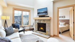 Una sala de estar acogedora con chimenea de piedra, un televisor montado encima y un espacio de descanso cómodo con sofá y sillones.