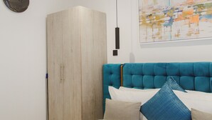 Een slaapkamer met een bed, een kledingkast, een hanglamp en een schilderij aan de muur.