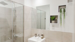 Een moderne badkamer met een glazen douchecabine, een witte wastafel en een toilet.