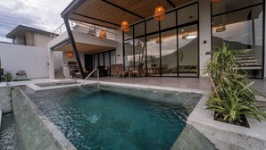 Area piscina esterna moderna con solarium in legno, lettini e zona pranzo con tavoli e sedie.