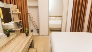 Ett hotellrum med en sminkbord i trä, en säng, en spegel, en hylla med krukväxter och en skjutdörr som leder till badrummet.