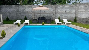 A rectangular swimming pool with a stone wall and a patio area with white lounge chairs and a table. - 3-bedroom villa in perfect Getamej with pool and coolest view (Ashtarak)