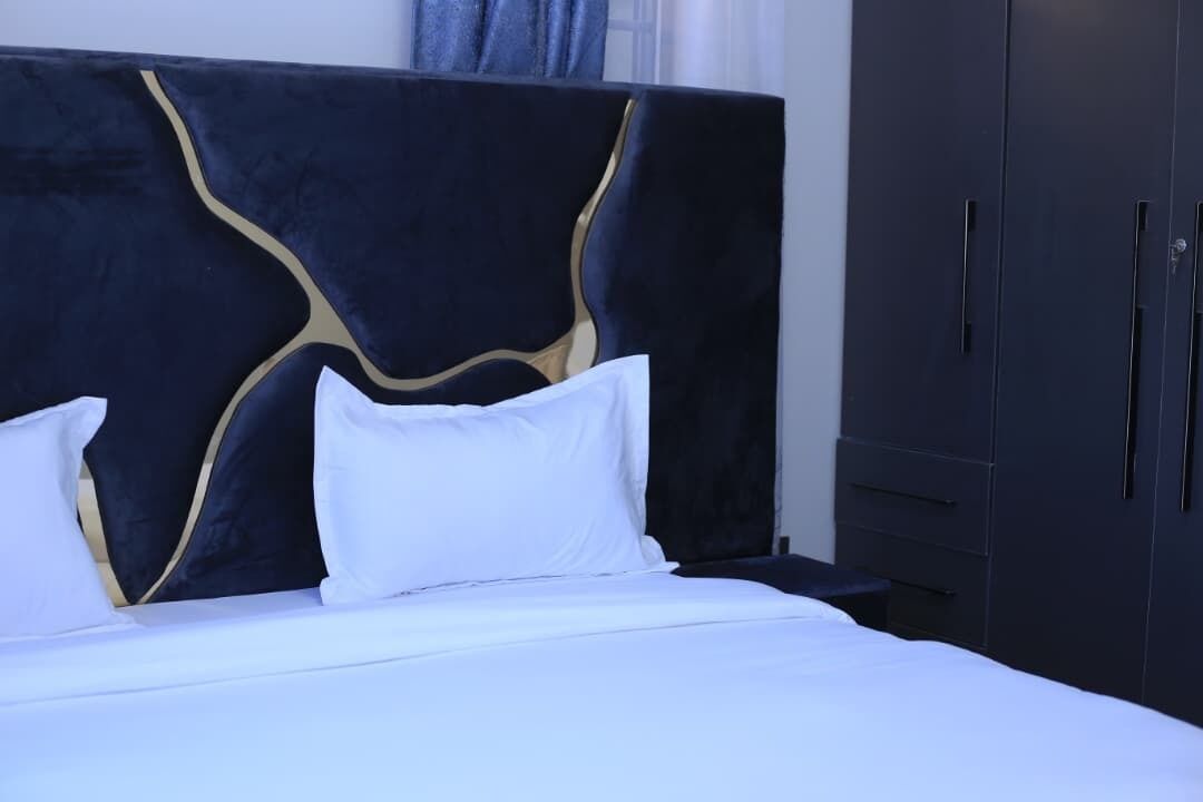 Ein Bett mit weißer Bettwäsche und einem dunklen Kopfteil mit goldenen Akzenten, ein Nachttisch und ein dunkler Kleiderschrank.