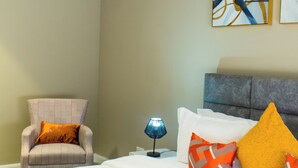 Una camera d'albergo con un letto, una sedia, una lampada e opere d'arte alle pareti.