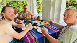 Un groupe de personnes est assis autour d’une table recouverte d’une nappe à rayures et prend son repas en plein air.
