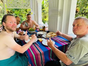 Eine Gruppe von Personen sitzt an einem Tisch mit kariertem Tuch und genießt eine Mahlzeit im Freien.