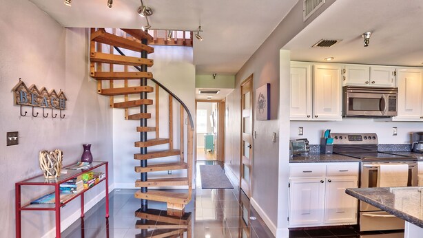 A modern kitchen with white cabinets, stainless steel appliances, and a wooden staircase. - 🐬Waterway Views🌞Quick Walk to Beach🌴Intercoastal #209 - Intercoastal Escape (Indian Shores)