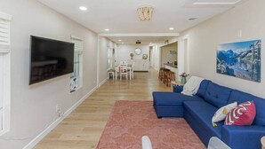 Un salon moderne avec un téléviseur à écran plat, un canapé bleu, un tapis rouge et un coin repas à l’arrière-plan.