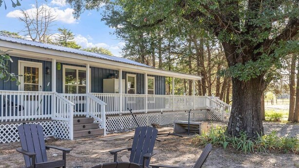 Une cabane dotée d’une véranda, d’un espace salon extérieur et d’un grand arbre.