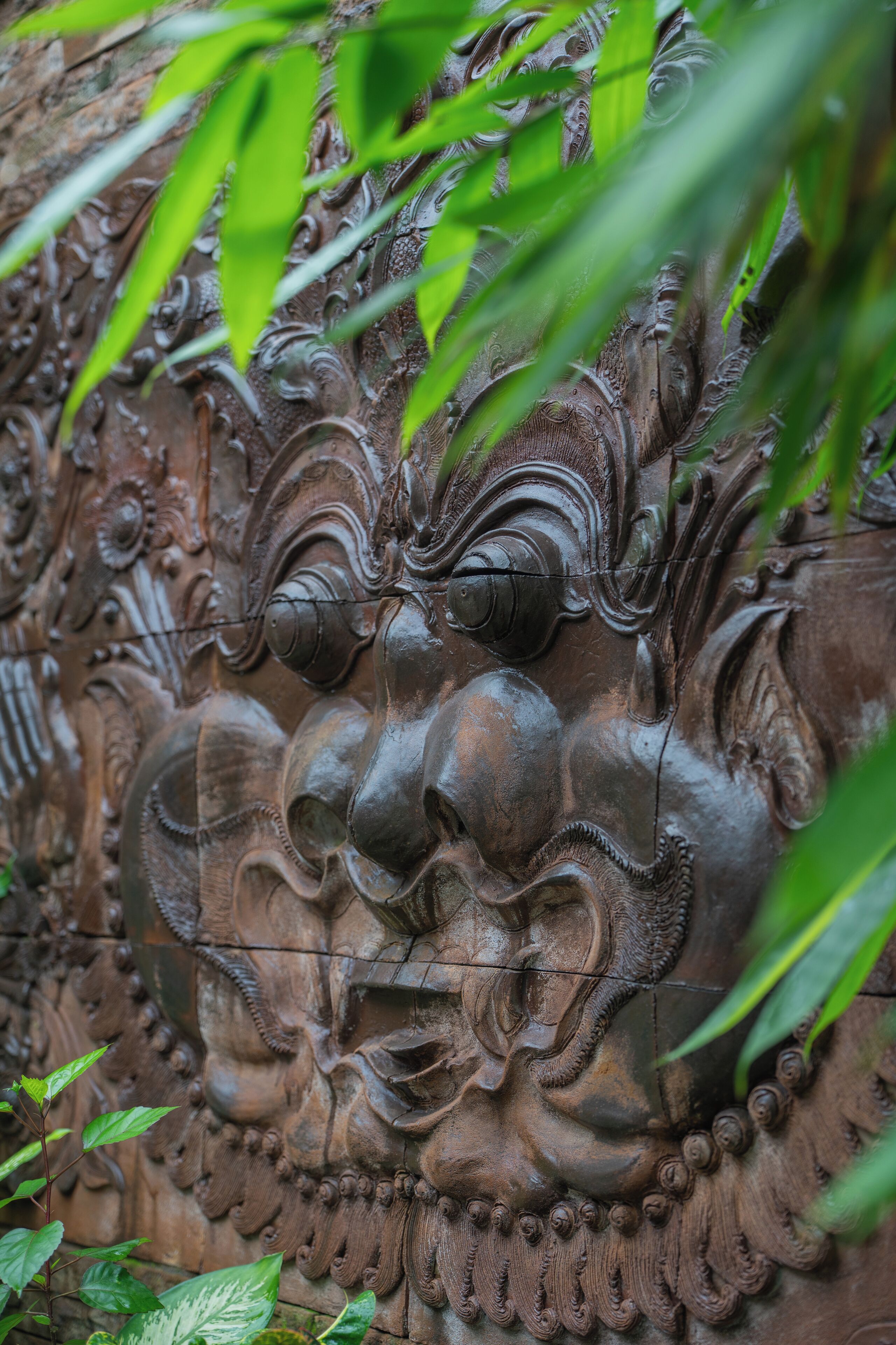 A detailed stone carving with intricate designs and foliage in the foreground.