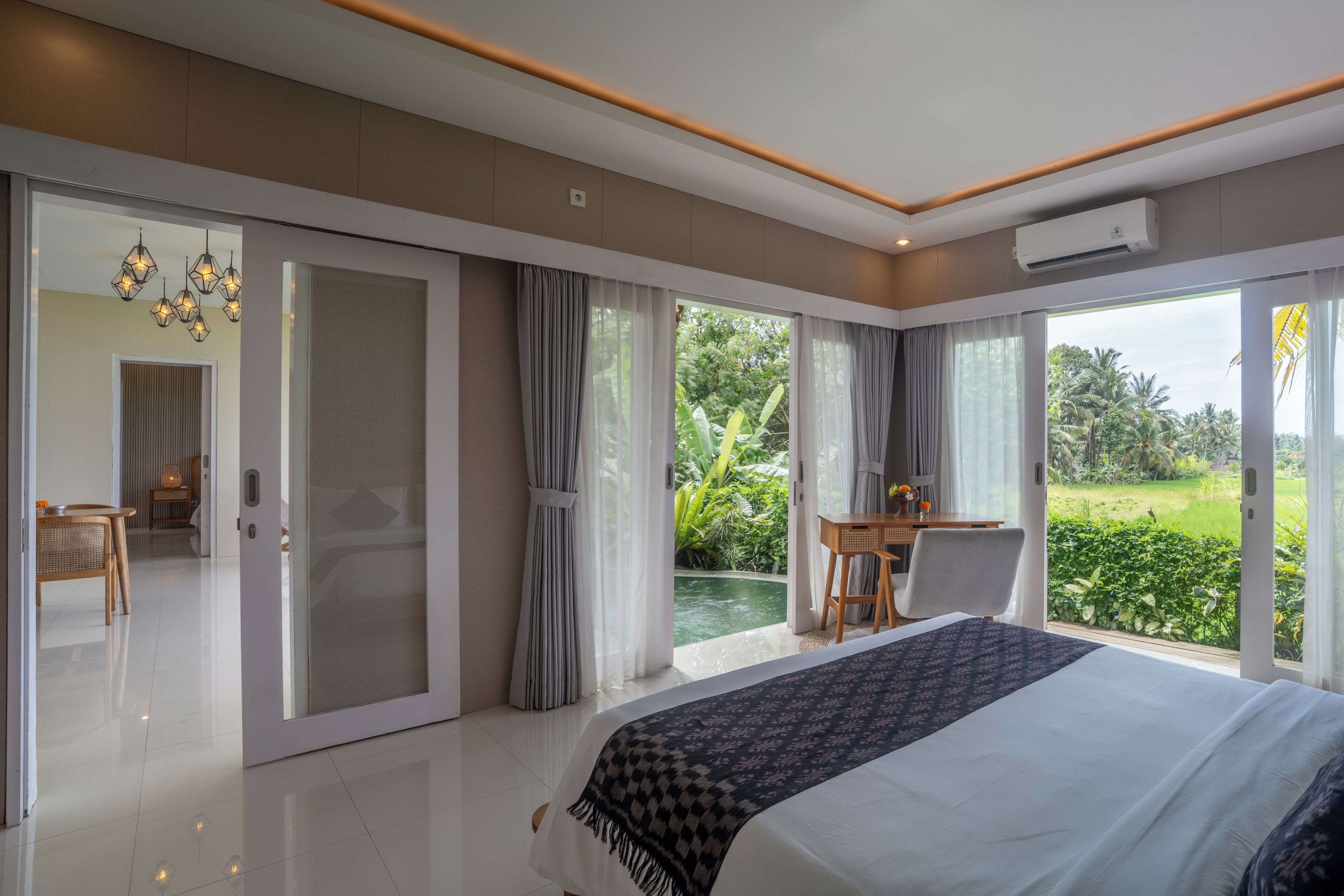 A modern hotel room with a large bed, a dining area, and a view of a lush garden.