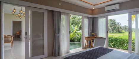 A modern hotel room with a large bed, a dining area, and a view of a lush garden.