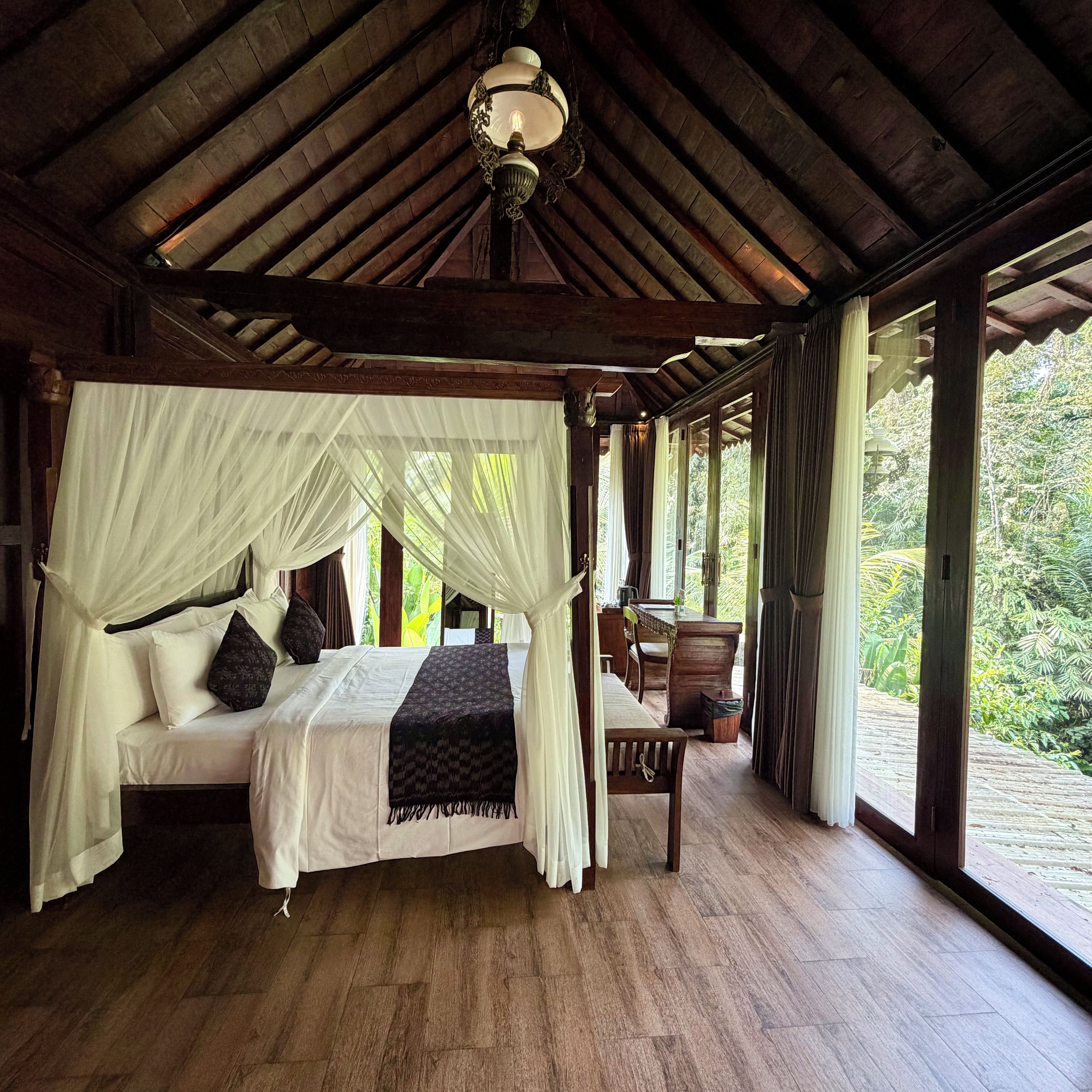 A four-poster canopy bed with a wooden floor and a view of the outdoors.