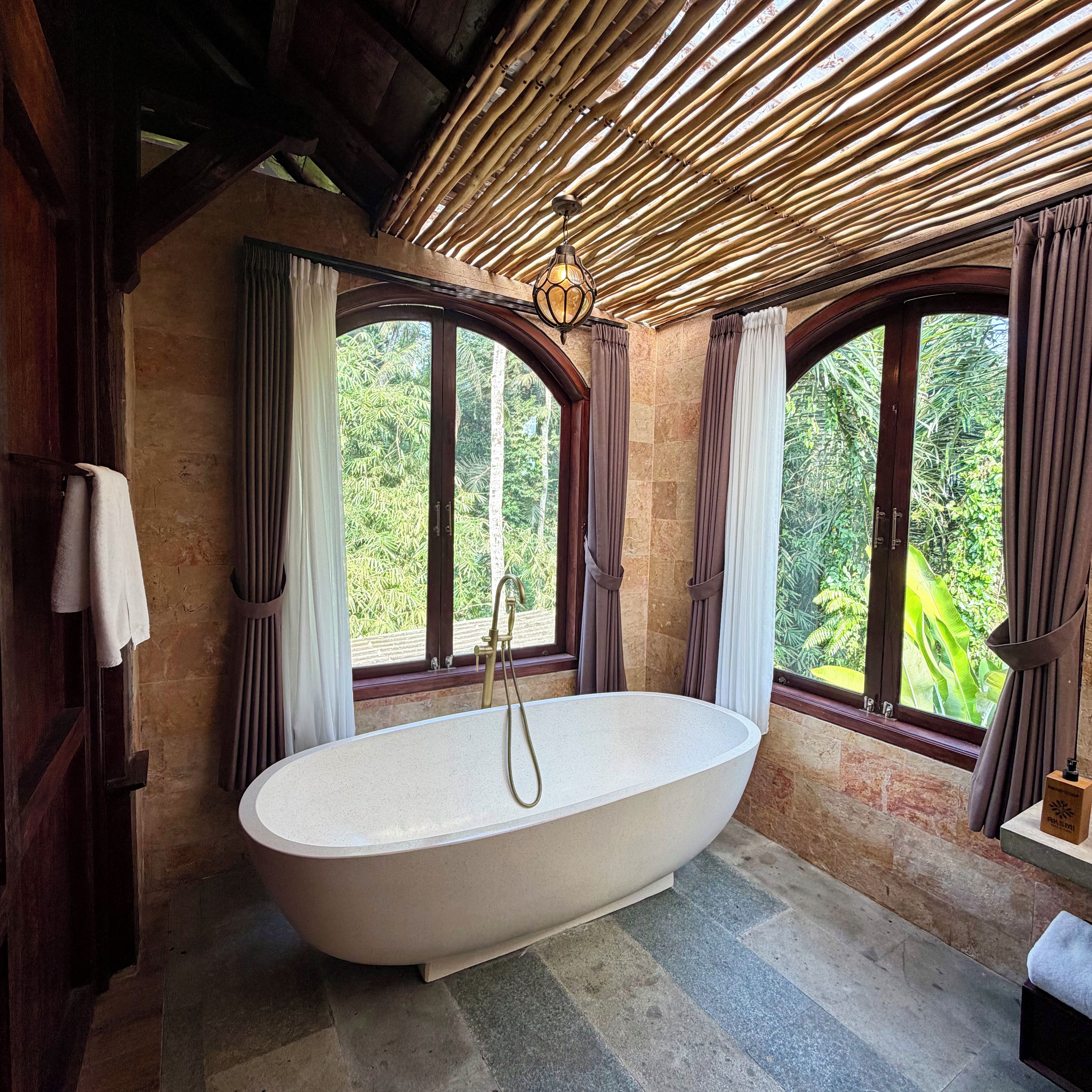 Un baño con una bañera independiente, ventanas amplias con cortinas y techo de madera.