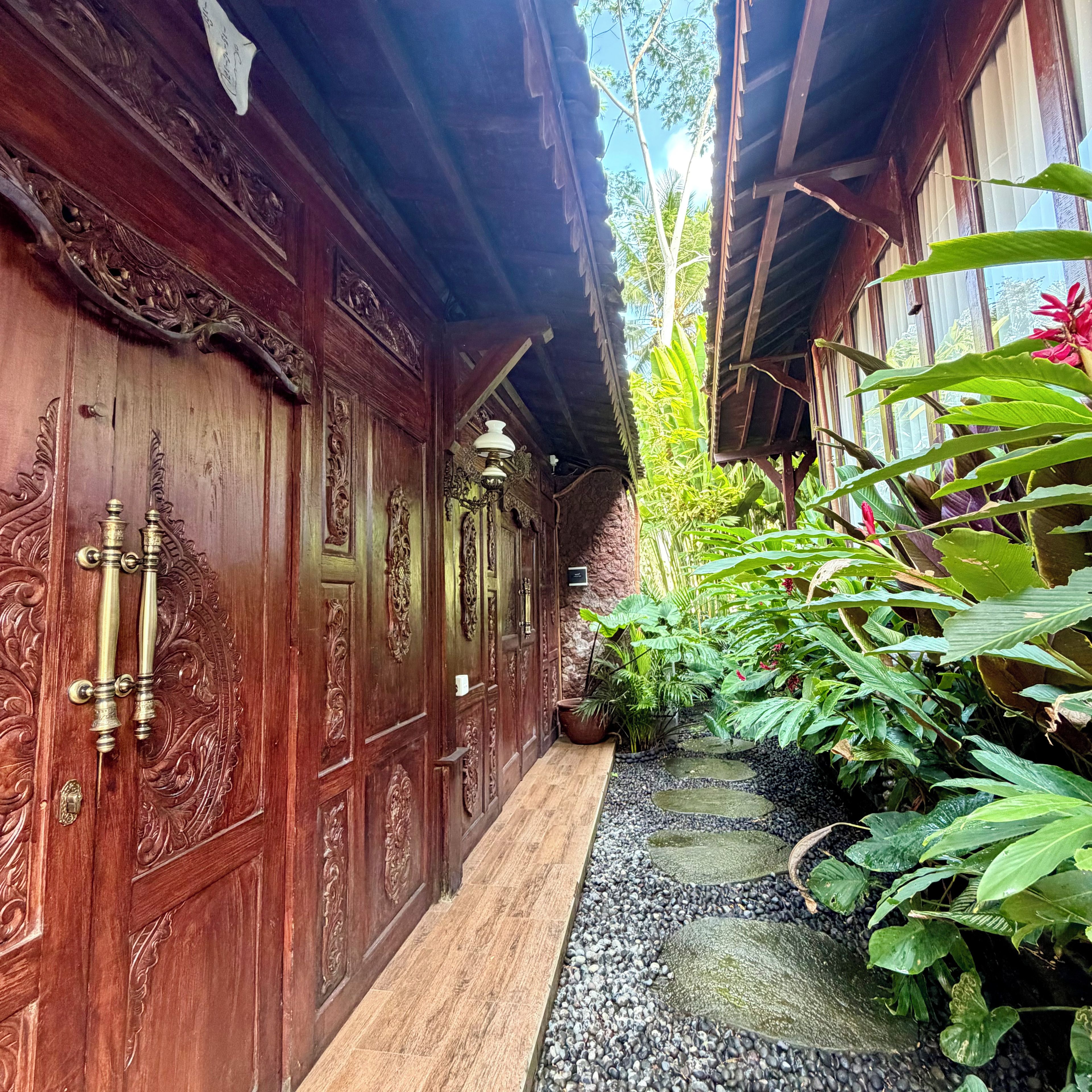 A wooden corridor with intricate carvings and a small garden area with a pebble path.