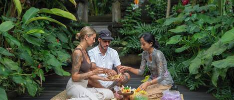 Three people sitting on a mat outdoors surrounded by lush greenery.
