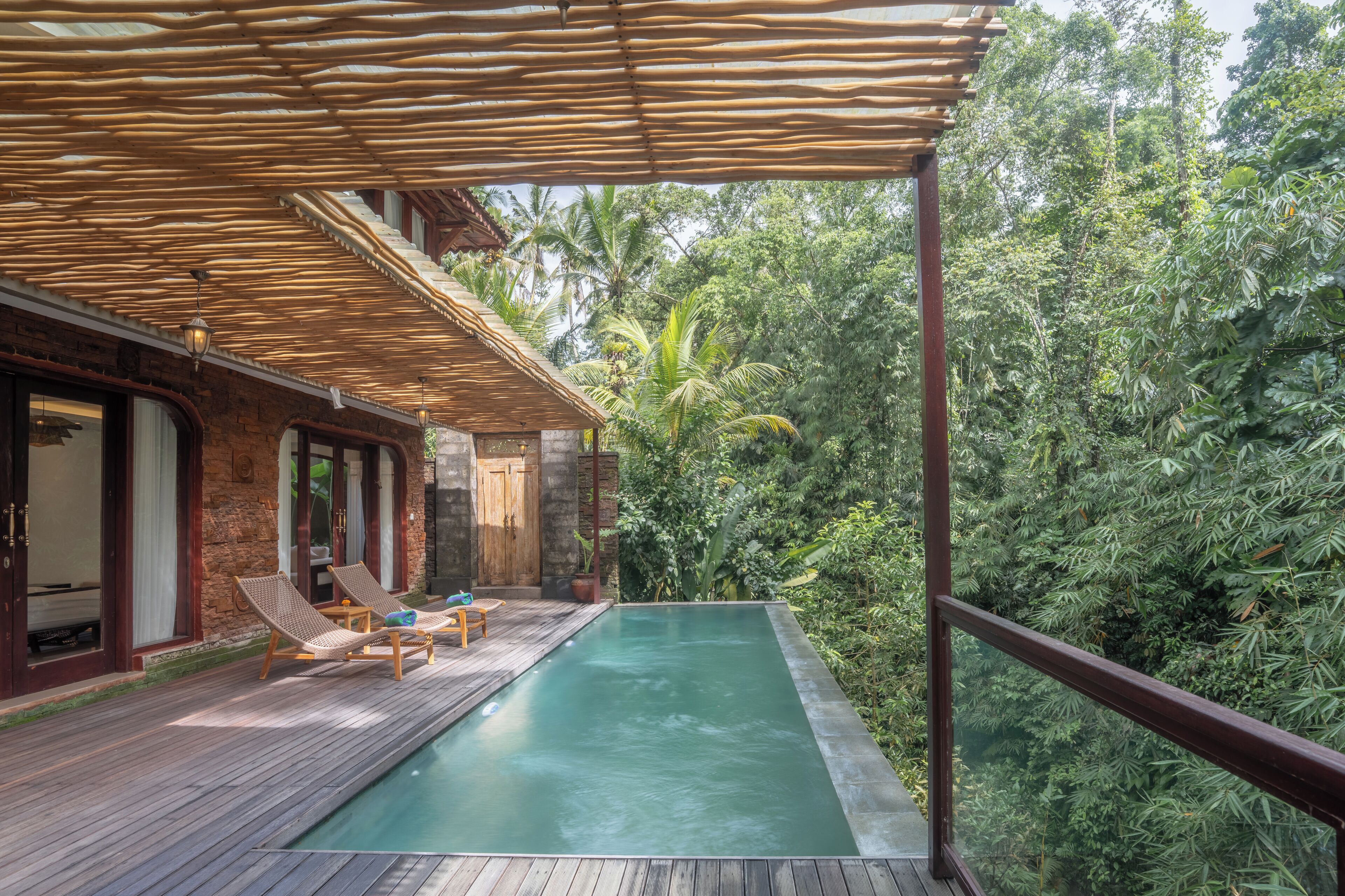 A wooden deck with a pool, lounge chairs, and a view of dense tropical foliage.