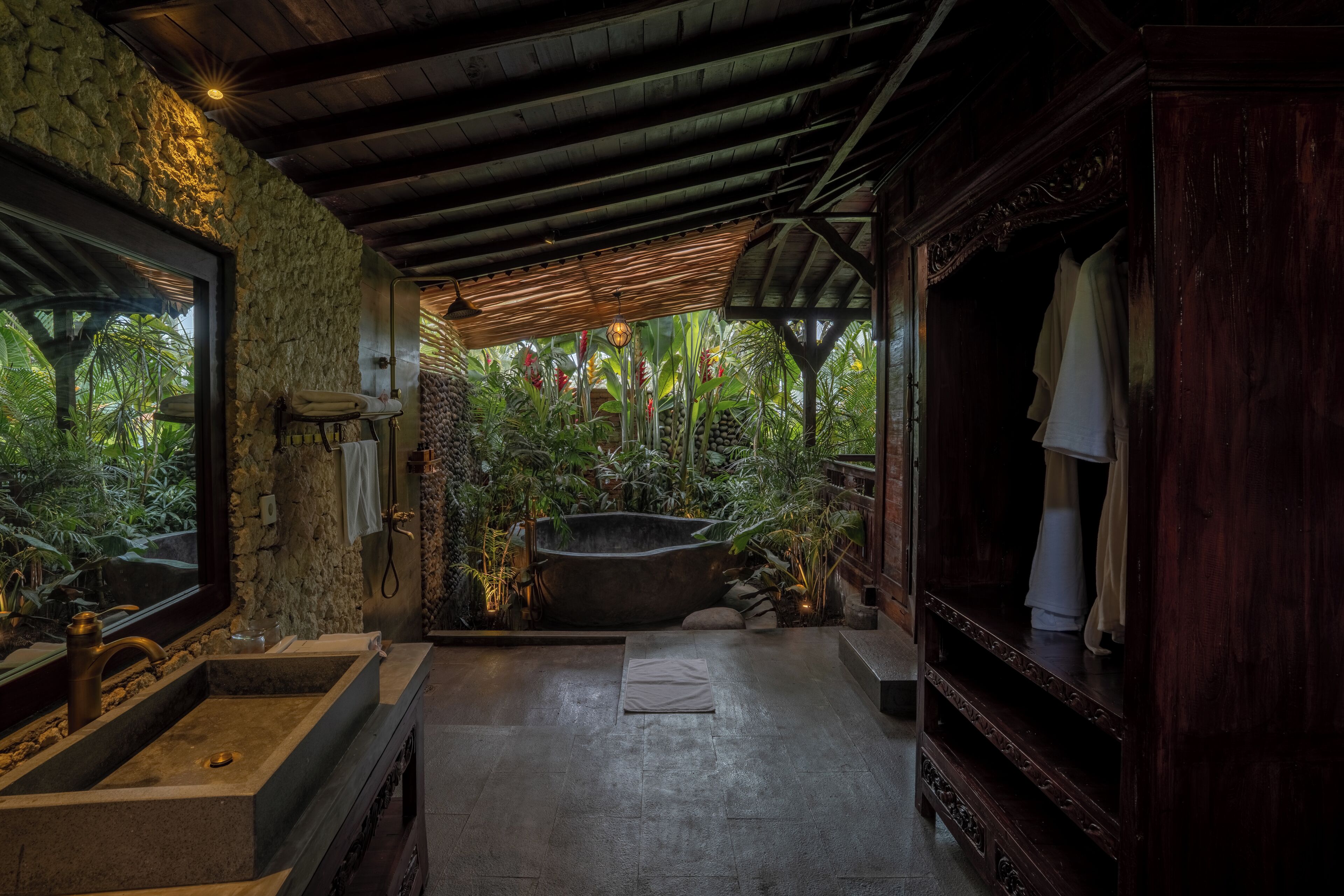 A bathroom with a stone wall, a large bathtub, and a wooden vanity.