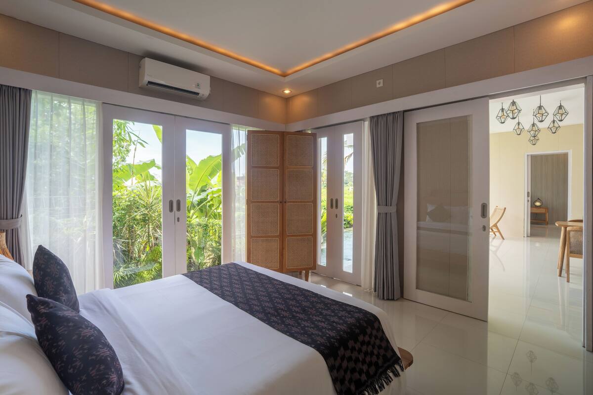 Een moderne slaapkamer met een groot bed, schuifdeuren naar een balkon en een eethoek die door de deuren zichtbaar is.