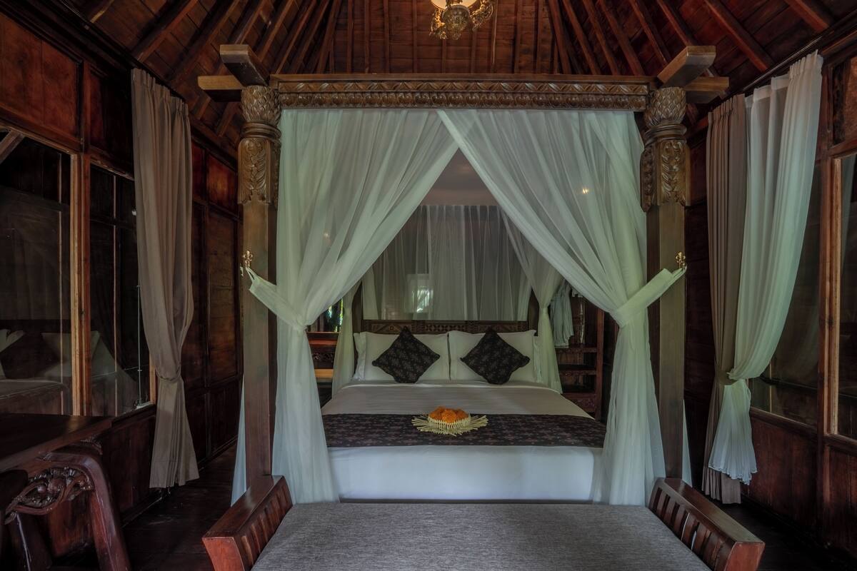 Een hemelbed met een wit laken en twee decoratieve kussens.
