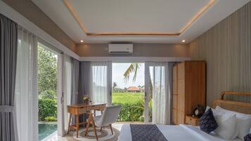 Un dormitorio con una cama grande, un escritorio con silla y vistas a un paisaje verde a través de amplios ventanales.
