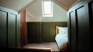 Ein Schlafzimmer mit schrägen Wänden, einem Oberlicht, einem Bett mit Holz Kopfteil und grünen Wandverkleidungen.