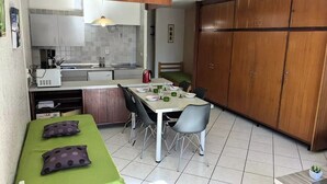 Eine kompakte Küche mit Essbereich, ein Bett mit grüner Bettwäsche und ein Holzschrank.