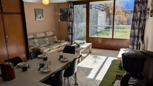 Ein Essbereich mit Tisch für vier Personen, einer Couch und Blick auf einen Garten durch eine Schiebetür.