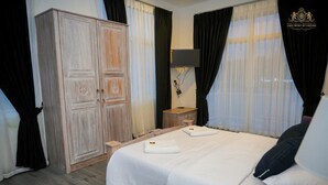 A hotel room with a large wardrobe, a bedside table with a lamp, and a bed with white linens.