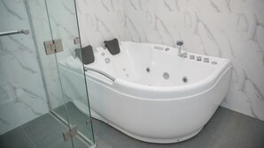 A modern bathroom with a large white bathtub, glass shower enclosure, and marble walls.
