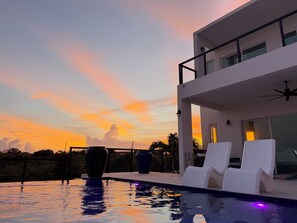 Una casa moderna con piscina, balcón y vistas al atardecer.