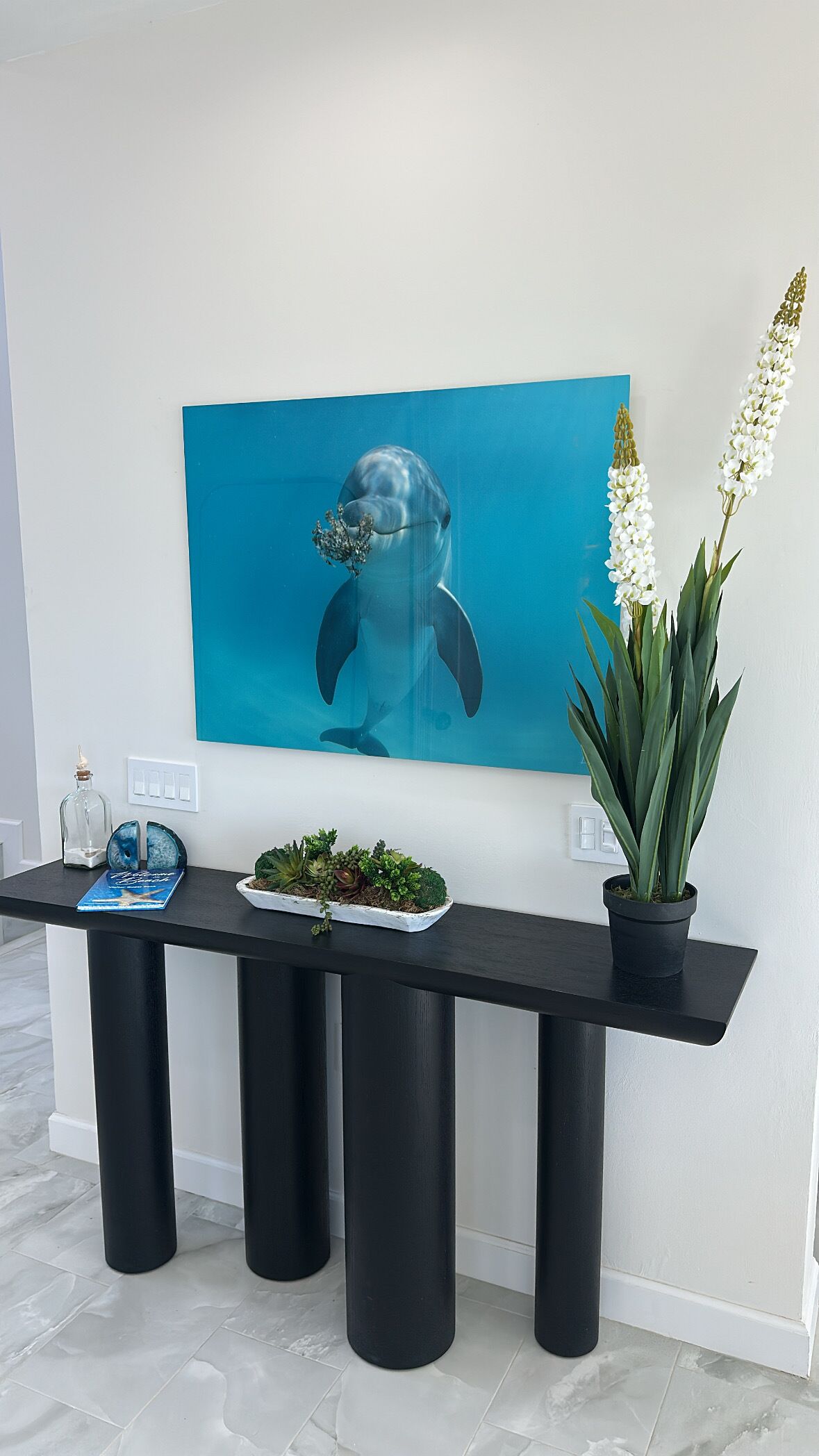Un comptoir d’accueil moderne agrémenté d’une œuvre d’art murale bleue représentant un dauphin, d’une plante en pot et d’un petit objet décoratif.