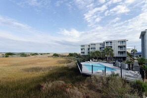 Ein modernes Hotel mit Schwimmbad, umgeben von einer naturnahen Landschaft und blauem Himmel.