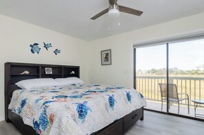 Ein Schlafzimmer mit Bett, Deckenventilator, Fenster und Blick ins Freie.