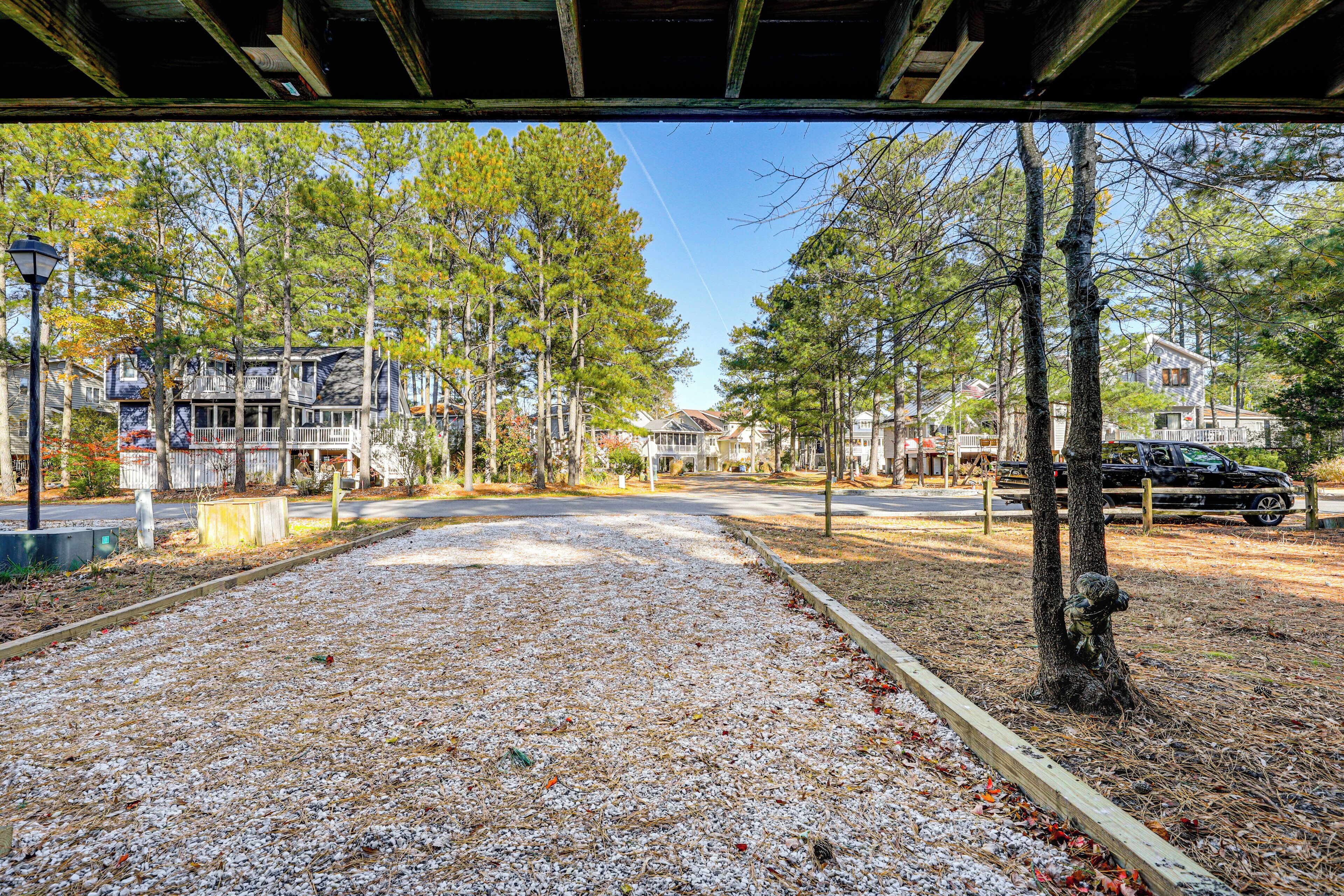 A covered walkway with gravel ground, surrounded by trees and residential buildings.