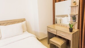 A hotel room with a bed, a wooden desk with a mirror, and a small shelf with plants. - Spacious Two Bedroom Luxury at Avant Garde (Accra)