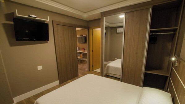 Habitación de hotel con cama, televisión montada en la pared, armario y un escritorio pequeño con silla.