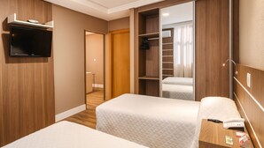Ein Hotelzimmer mit zwei Betten, einem an der Wand befestigten Fernseher, einem Holzschrank und einem Schiebetürenkleiderschrank.
