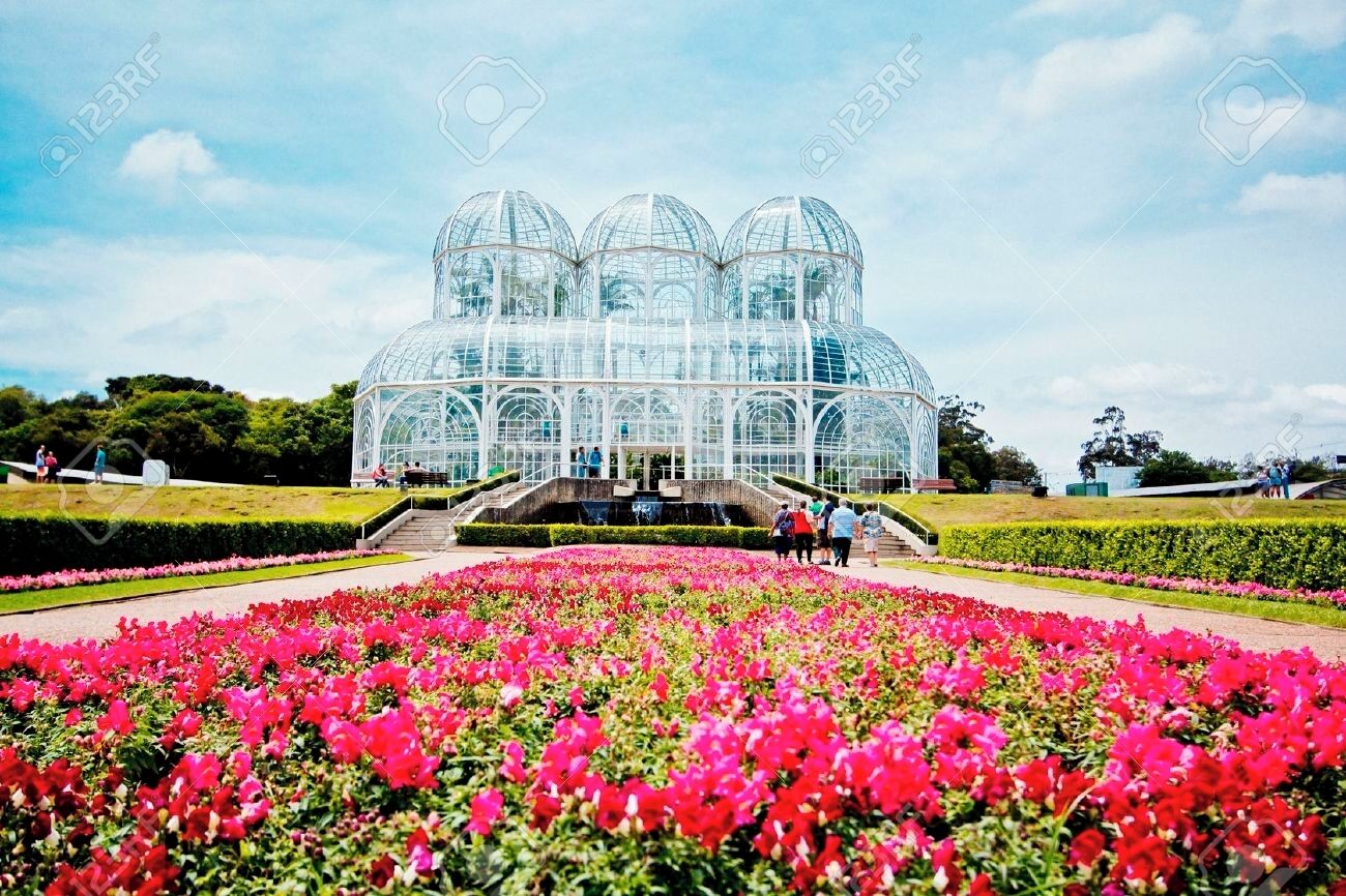 Ett växthus med en kupolformad glasstruktur, omgivet av en trädgård med rosa blommor.