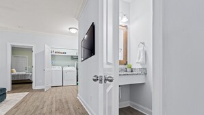 A modern, well-lit room with a wooden floor, a built-in washer and dryer, a large mirror, and a flat-screen TV mounted on the wall. - Charming 3-bedroom, 2.5 bath townhome. Largest with accommodations in Florence. (Florence)
