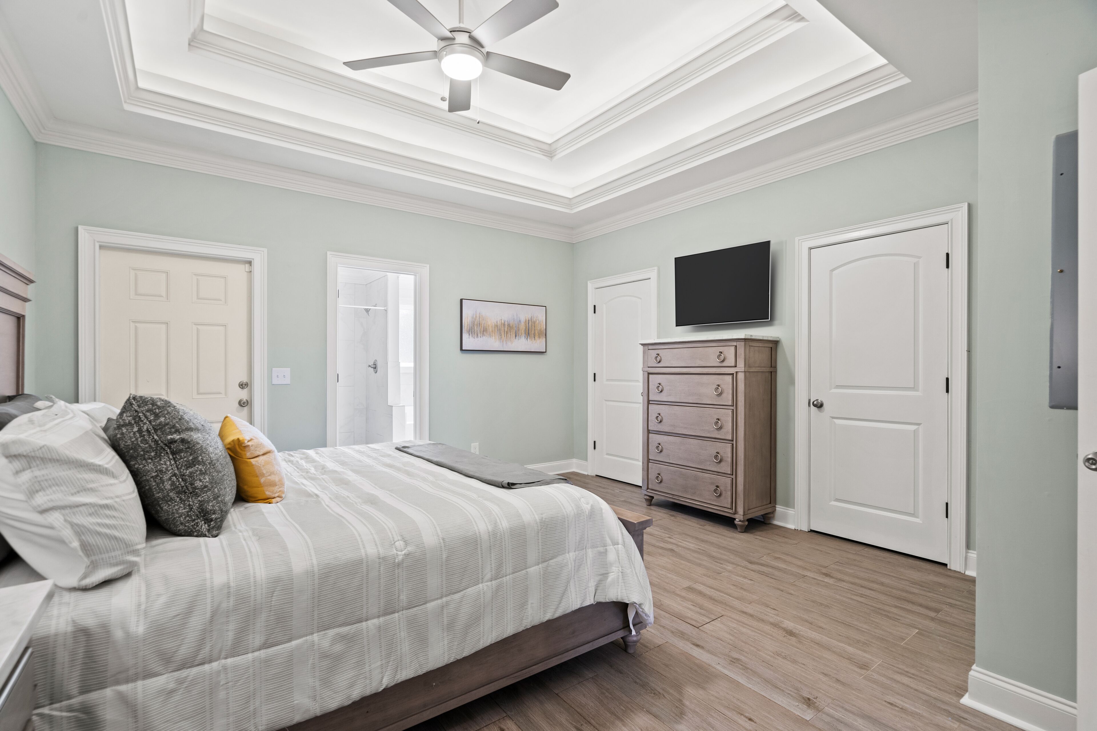 A bedroom with a bed, a dresser, a television, and a ceiling fan.