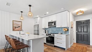 A modern kitchen with white cabinets, a central island with bar stools, stainless steel appliances, and a blue tiled backsplash. - New to 30A! Freshly Renovated, Walk to Seaside, Pool, Easy Beach Access (Santa Rosa Beach)