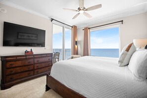 Ein Schlafzimmer mit einem großen Bett, einem Schminktisch, einem Deckenventilator, einem an der Wand montierten Fernseher und Blick aufs Meer.
