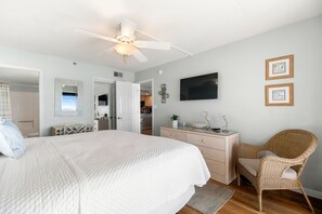 A bedroom with a large bed, a ceiling fan, a dresser, a wicker chair, and a flat-screen TV on the wall. - Ocean Breeze 505 - NEW LISTING!! Gulf front, Updated Condo! (Perdido Key)