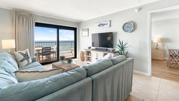 A living room with a sofa, TV, and a balcony with a view. - Ocean Breeze 505 - NEW LISTING!! Gulf front, Updated Condo! (Perdido Key)